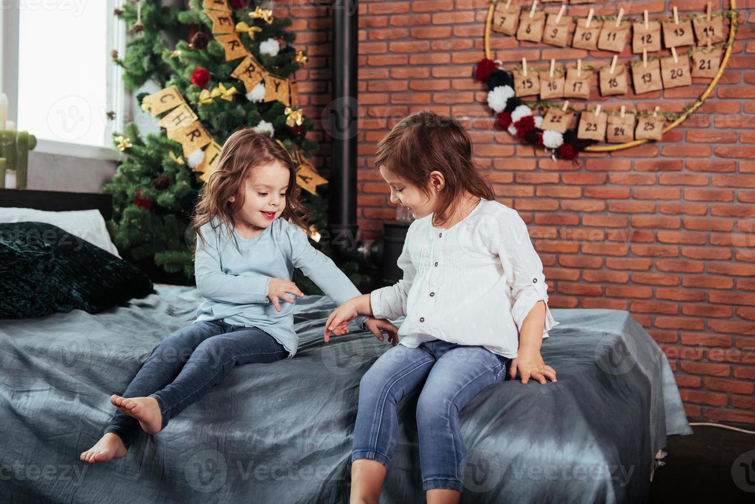 passando o tempo brincando um com o outro enquanto espera o natal. crianças senta-se na cama com fundo decorativo. concepção de ano novo foto
