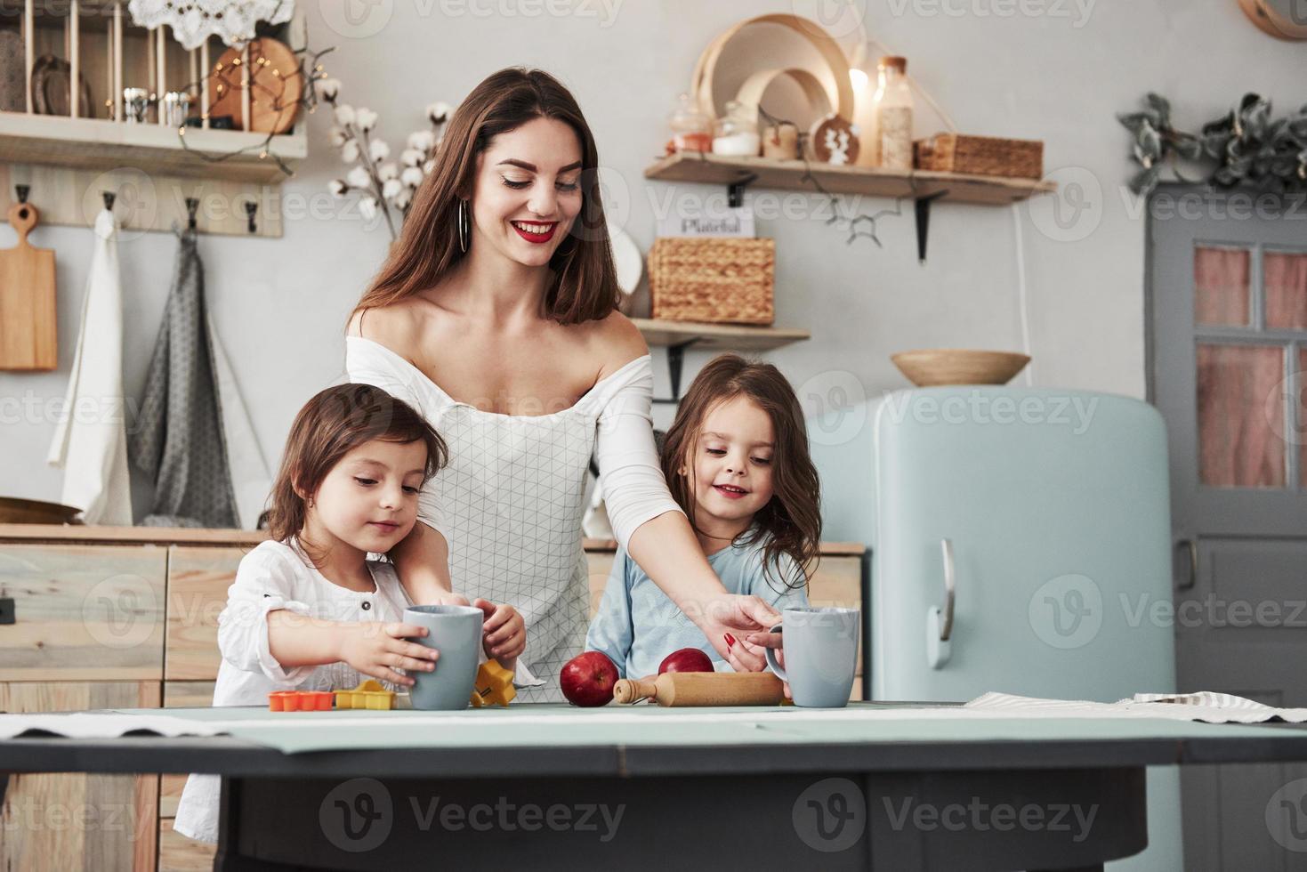 garota vai tentar suco nutricional. jovem mulher bonita dá bebidas às crianças enquanto elas estão sentadas perto da mesa com brinquedos foto