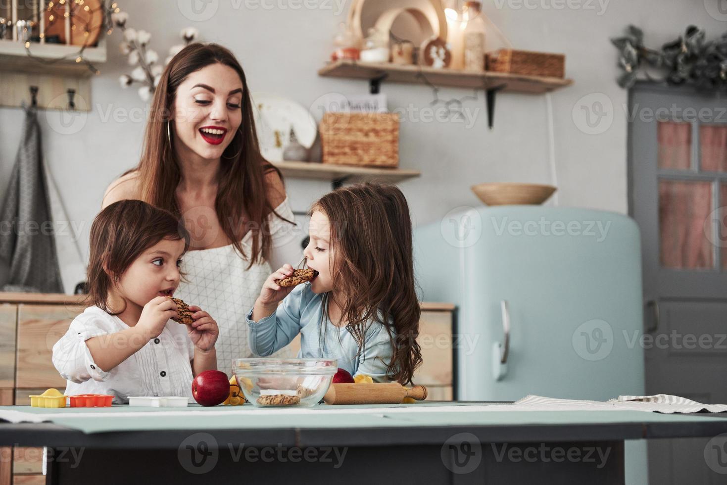 processo de comer. jovem mulher bonita dá os biscoitos enquanto eles estão sentados perto da mesa com brinquedos foto