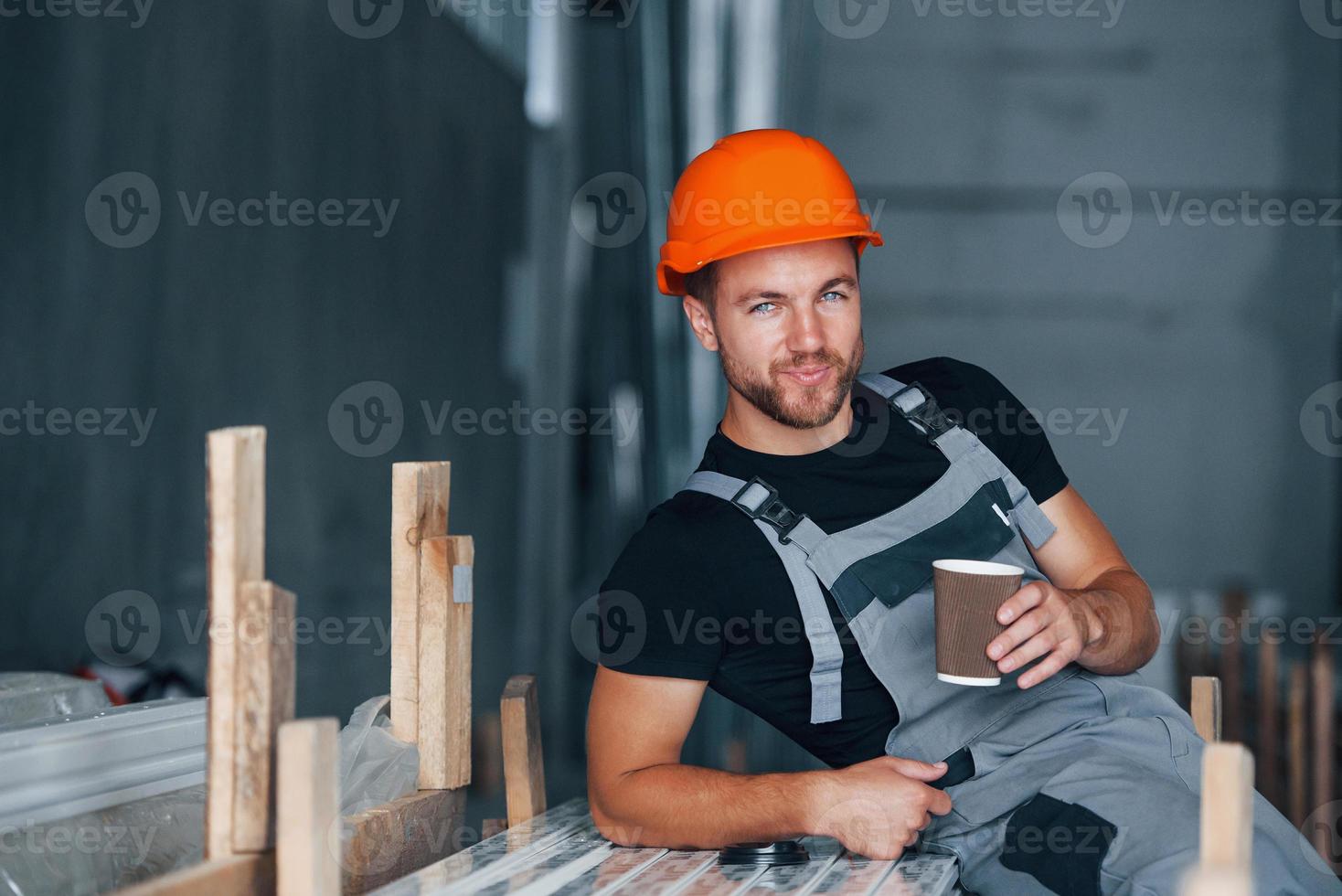 com copo de bebida. pausa para almoço. trabalhador industrial dentro de casa na fábrica. jovem técnico com capacete laranja foto