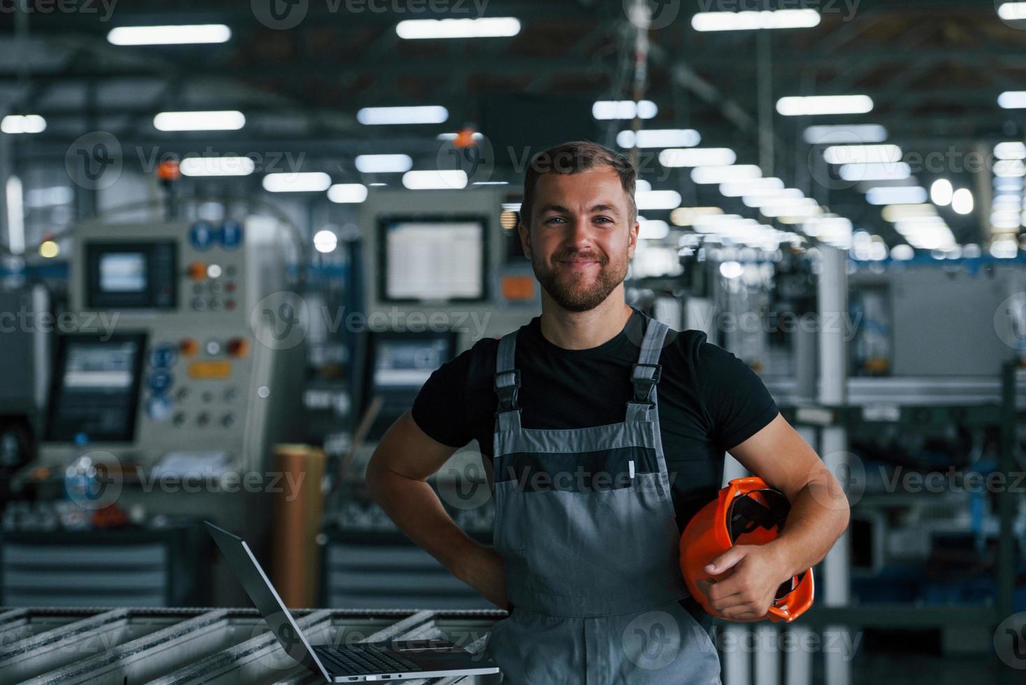 retrato de trabalhador industrial dentro de casa na fábrica. jovem técnico com capacete laranja foto