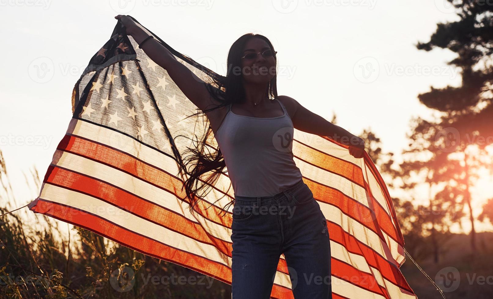 Linda luz. morena com bandeira dos eua nas mãos se diverte e sente liberdade ao ar livre em dia de sol foto