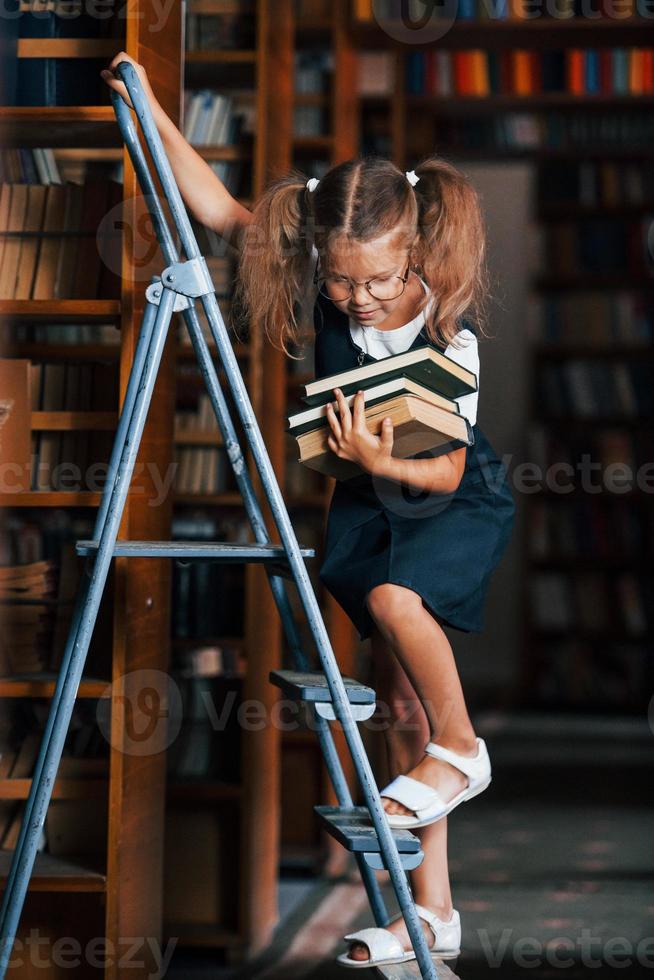 menina da escola na escada na biblioteca cheia de livros. concepção de educação foto