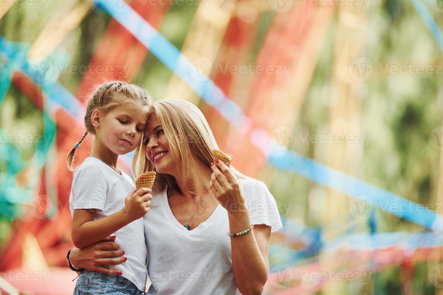 tomando sorvete. menina alegre sua mãe se diverte no parque juntos perto de atrações foto