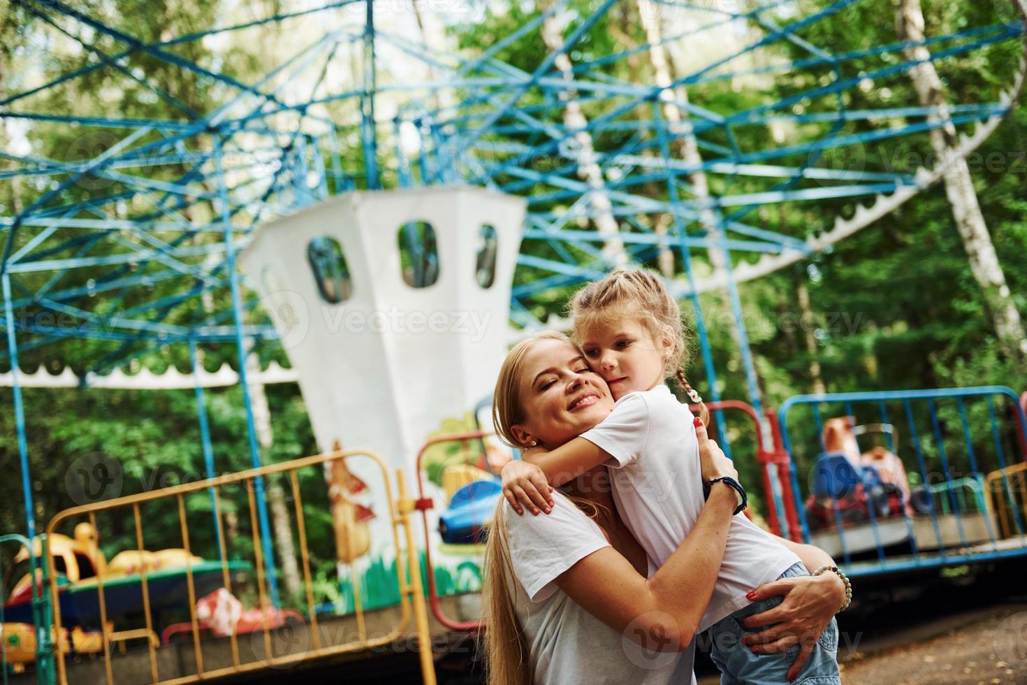 amando um ao outro. menina alegre sua mãe se diverte no parque juntos perto de atrações foto