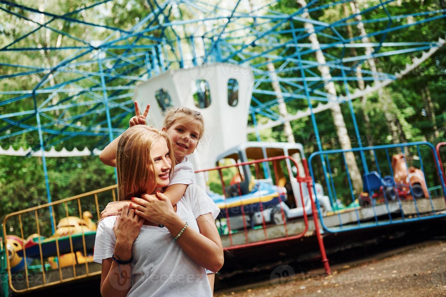 amando um ao outro. menina alegre sua mãe se diverte no parque juntos perto de atrações foto