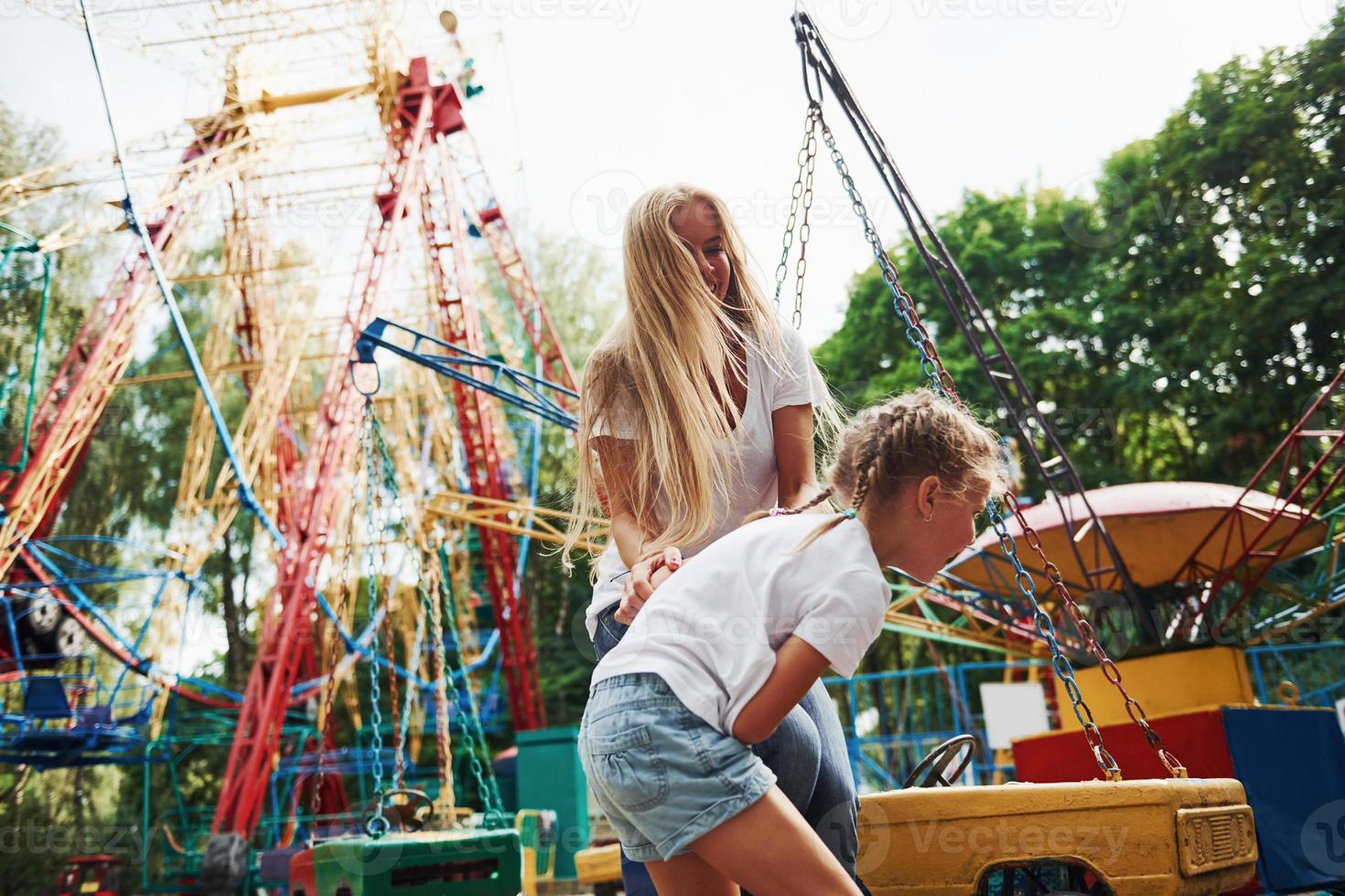 correndo e brincando. menina alegre sua mãe se diverte no parque juntos perto de atrações foto