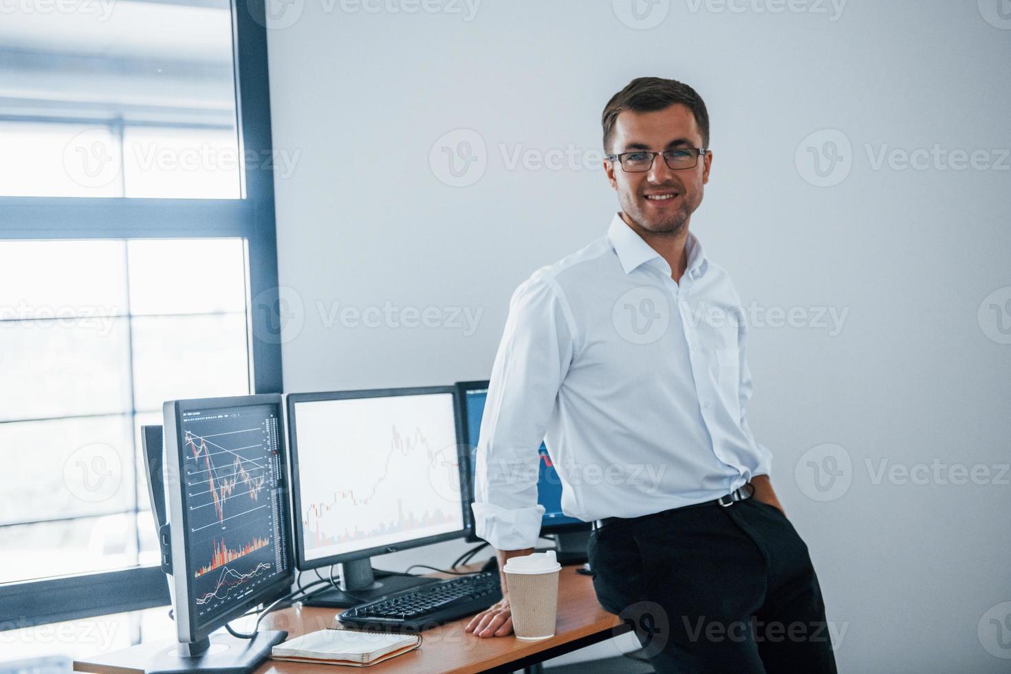 empregado feliz. jovem empresário em roupas formais está no escritório com várias telas. concepção de troca e dinheiro foto