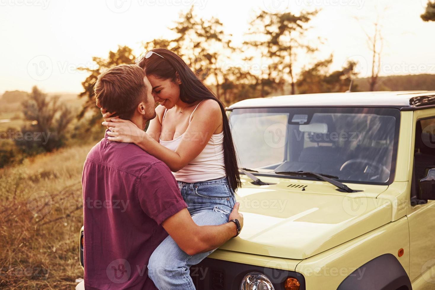 lindo casal beijando ao ar livre. menina senta-se no jipe verde. linda tarde ensolarada foto