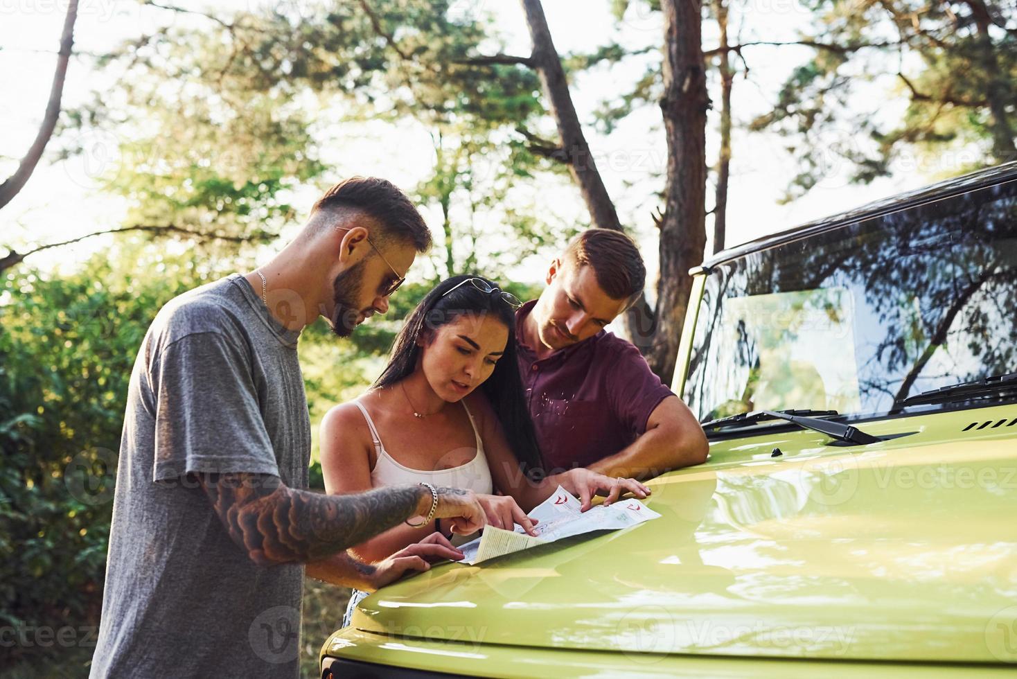 jovens amigos lendo o mapa que está no capô do jipe verde moderno na floresta foto