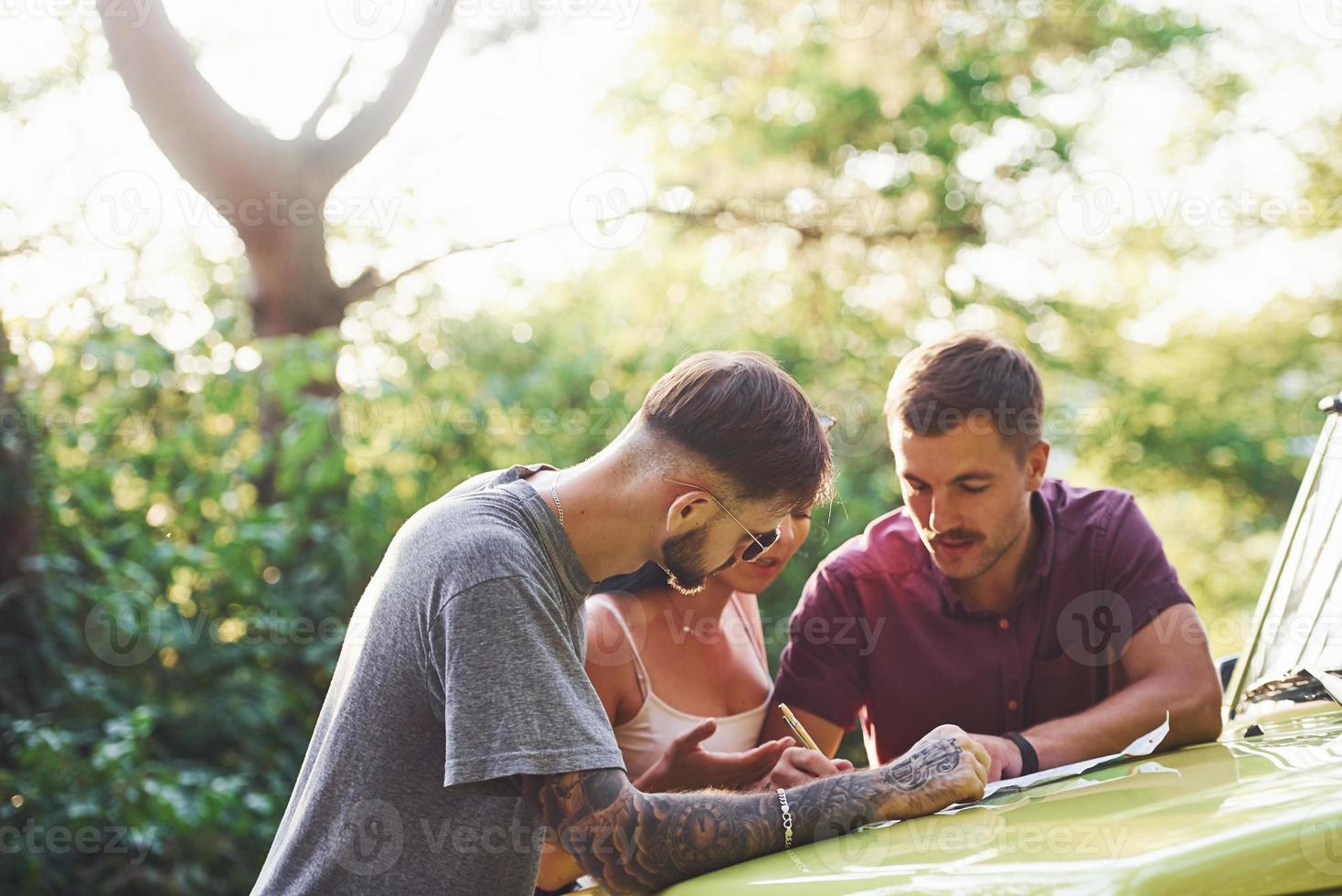 jovens amigos lendo o mapa que está no capô do jipe verde moderno na floresta foto