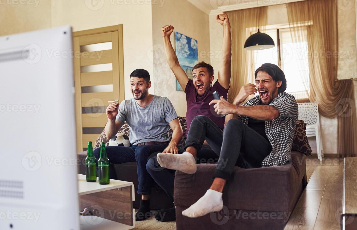 comemorando a vitória. três amigos animados assistindo futebol na tv em casa juntos foto