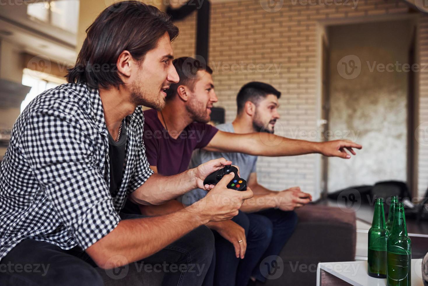 vista lateral. grupo de amigos se diverte jogando jogo de console dentro de casa na sala de estar foto