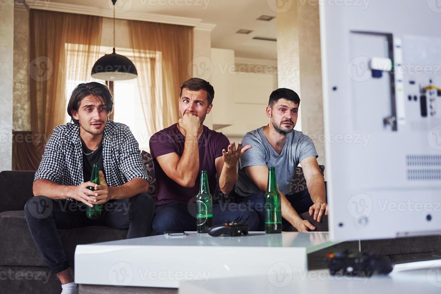 é uma derrota. tristes três amigos assistindo futebol na tv em casa juntos foto