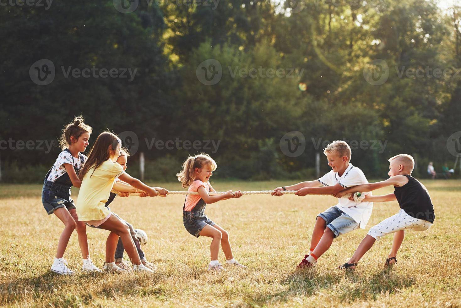 crianças jogando jogo de cabo de guerra no belo prado em dia ensolarado foto