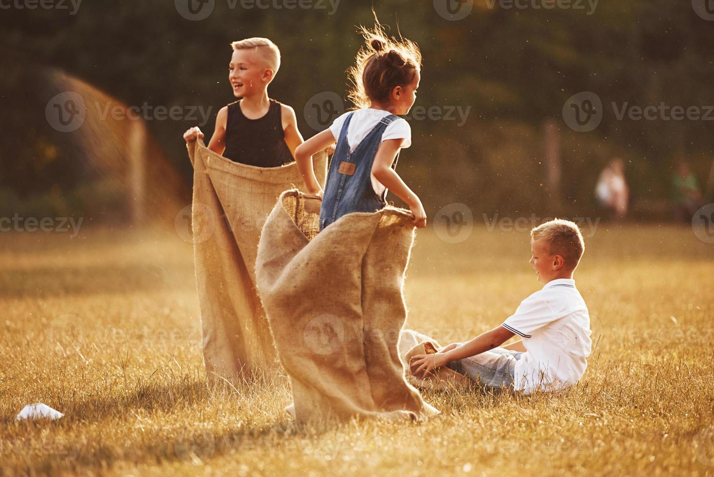 pulando a corrida de saco ao ar livre no campo. as crianças se divertem no dia ensolarado foto