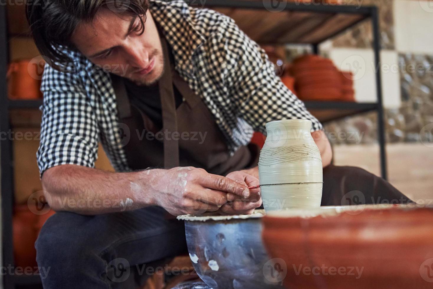 faz linhas com a ferramenta. ceramista usa roda de oleiro e cria um produto de argila artesanal foto