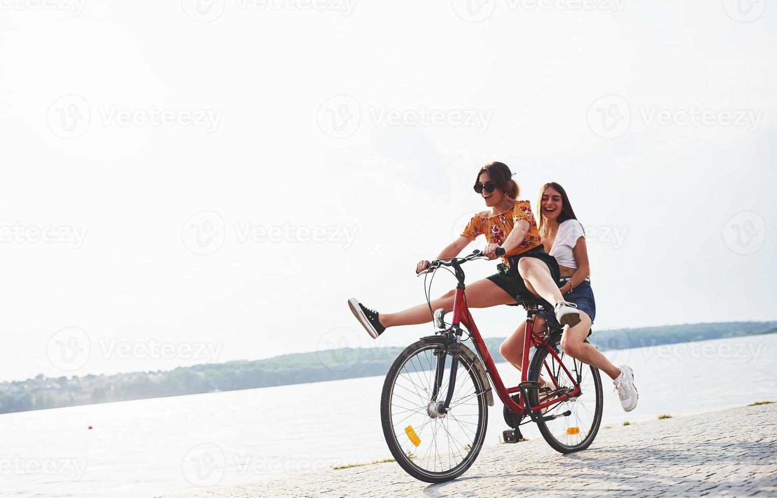 duas amigas na bicicleta se divertem na praia perto do lago foto