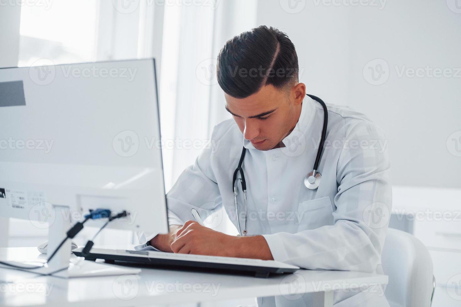trabalhando com documentos. jovem médico masculino elegante com estetoscópio está na clínica durante o dia foto