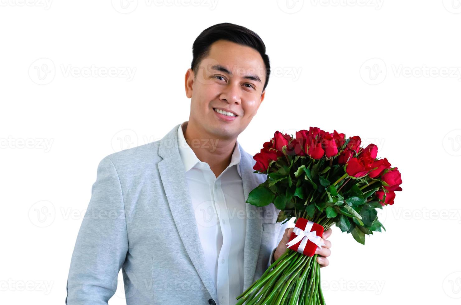 homem asiático vestindo terno cinza segurando um buquê de rosas vermelhas e caixa de presente vermelha isolada no fundo branco para o conceito de aniversário ou dia dos namorados. foto