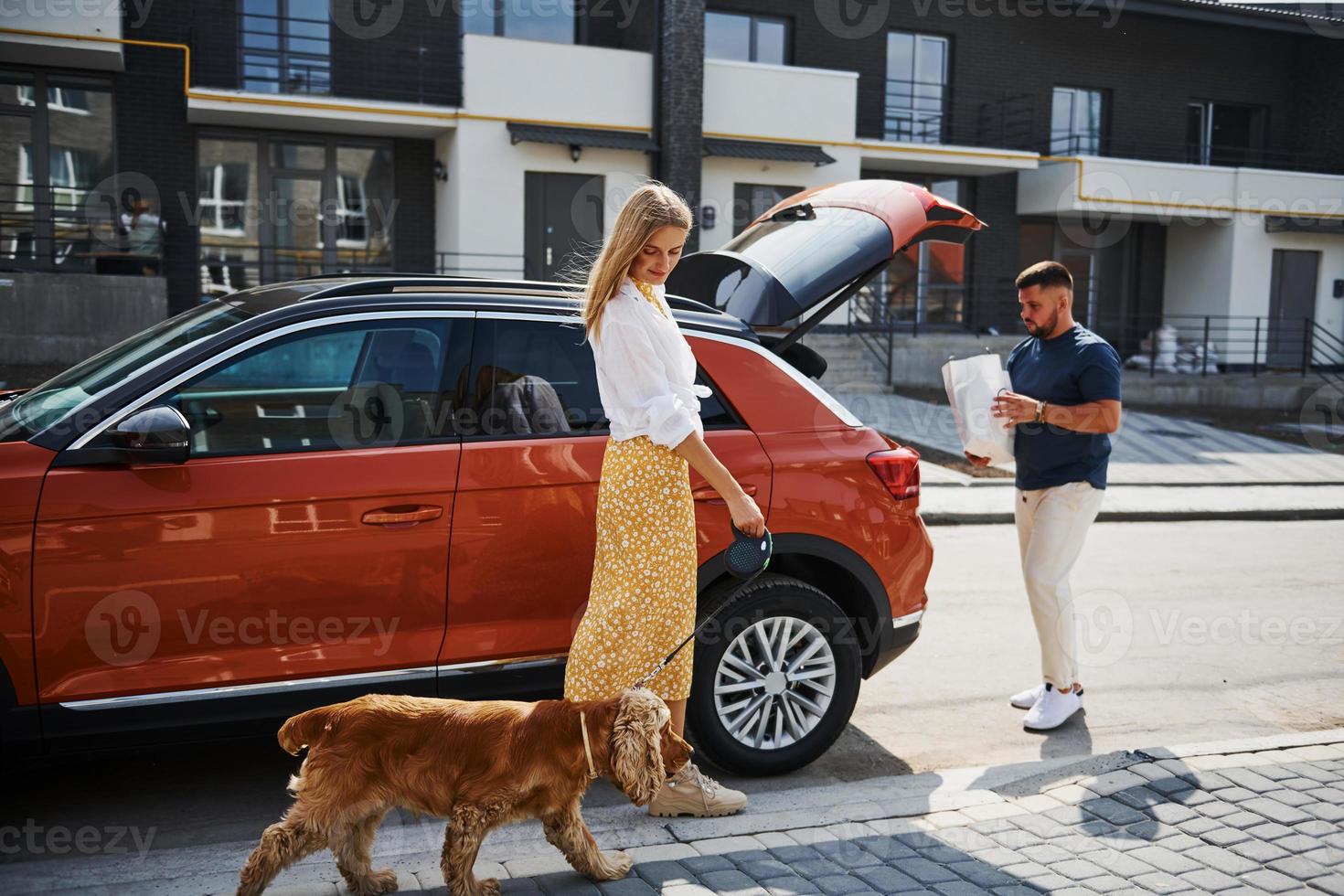 porta-malas está aberto. lindo casal tem um passeio junto com cachorro ao ar livre perto do carro foto