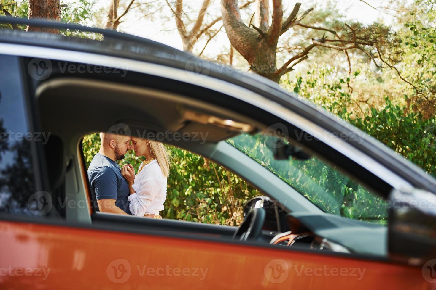 casal se abraçando na floresta perto de carro moderno foto