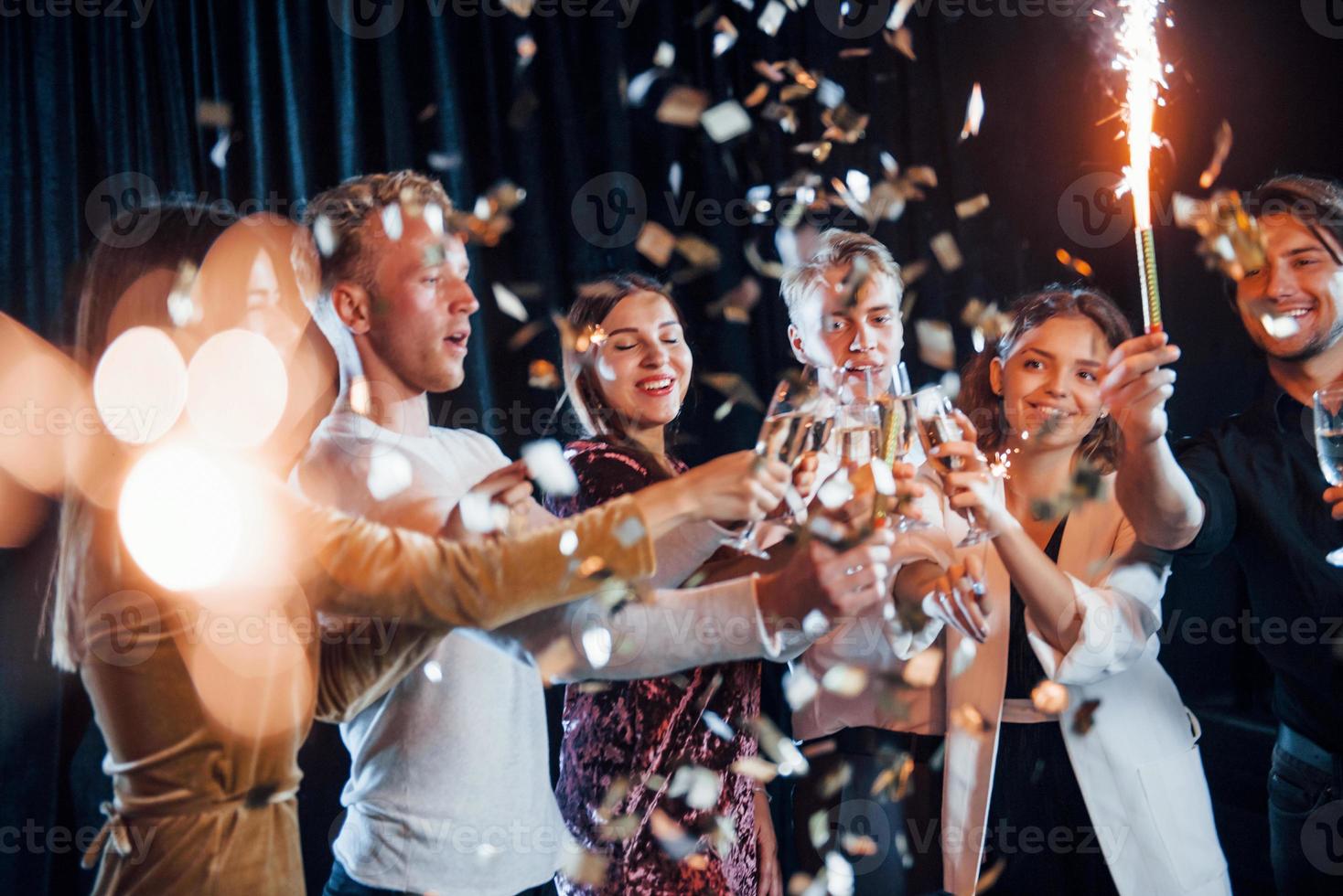 copos batendo. grupo de amigos alegres comemorando o ano novo dentro de casa com bebidas nas mãos foto