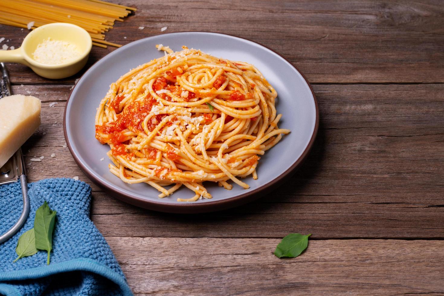 deliciosa massa de queijo espaguete servida em um prato legumes, molho de tomate italiano e especiarias dispostas em uma mesa de madeira, vista superior foto