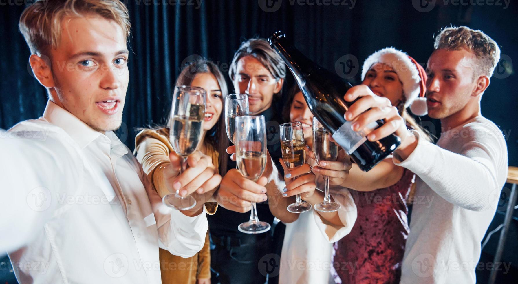 tira selfie. grupo de amigos alegres comemorando o ano novo dentro de casa com bebidas nas mãos foto