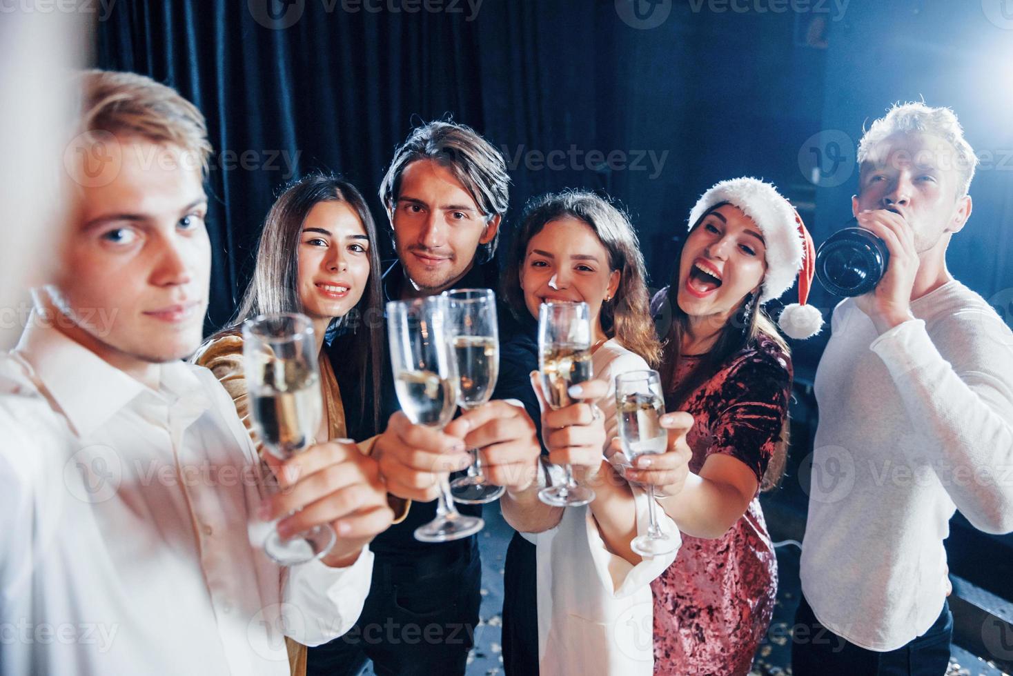 tira selfie. grupo de amigos alegres comemorando o ano novo dentro de casa com bebidas nas mãos foto