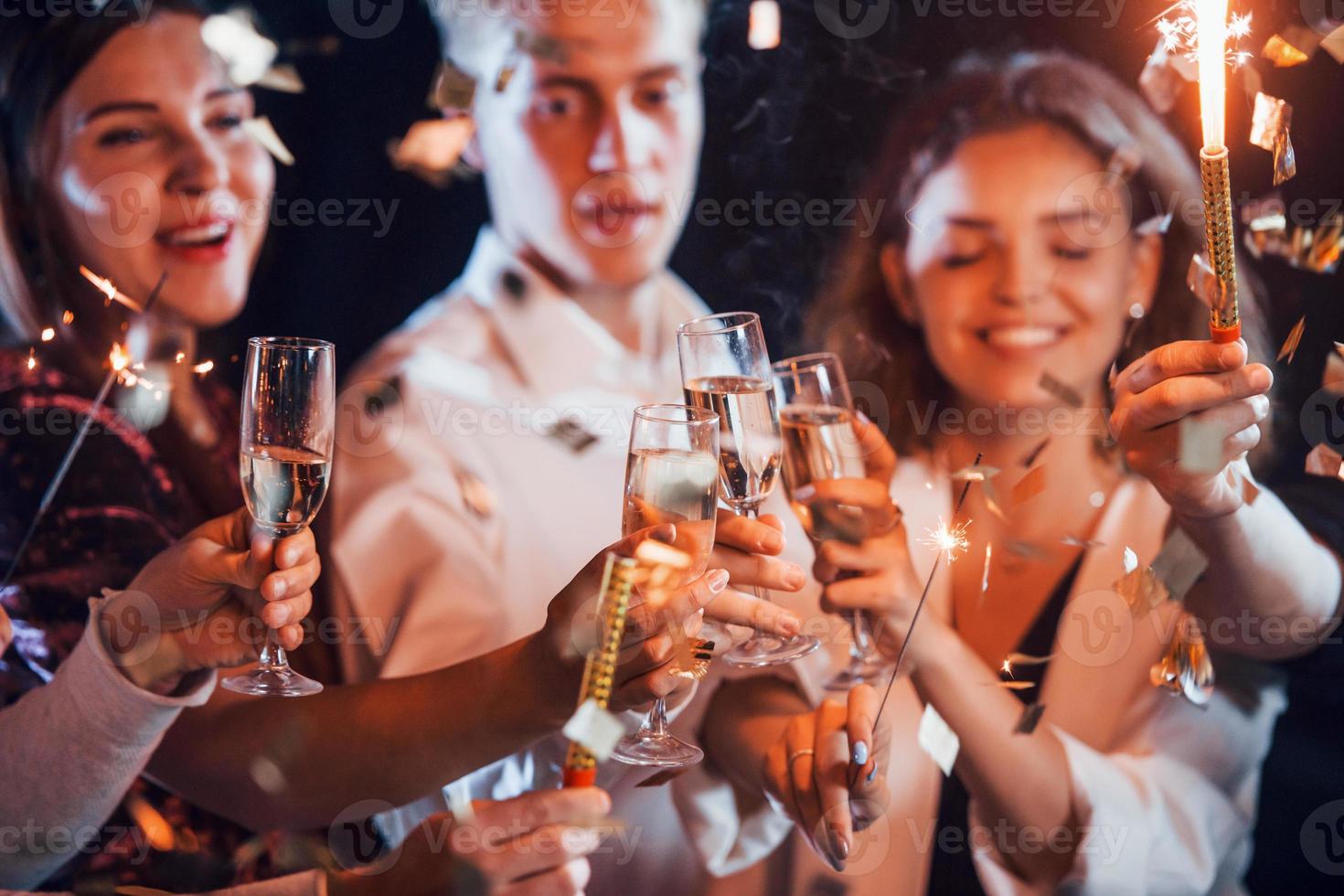 copos batendo. grupo de amigos alegres comemorando o ano novo dentro de casa com bebidas nas mãos foto