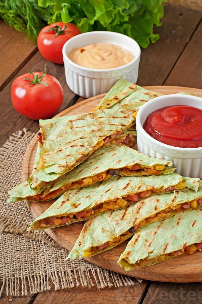 quesadilla mexicano fatiado com legumes e molhos em cima da mesa foto