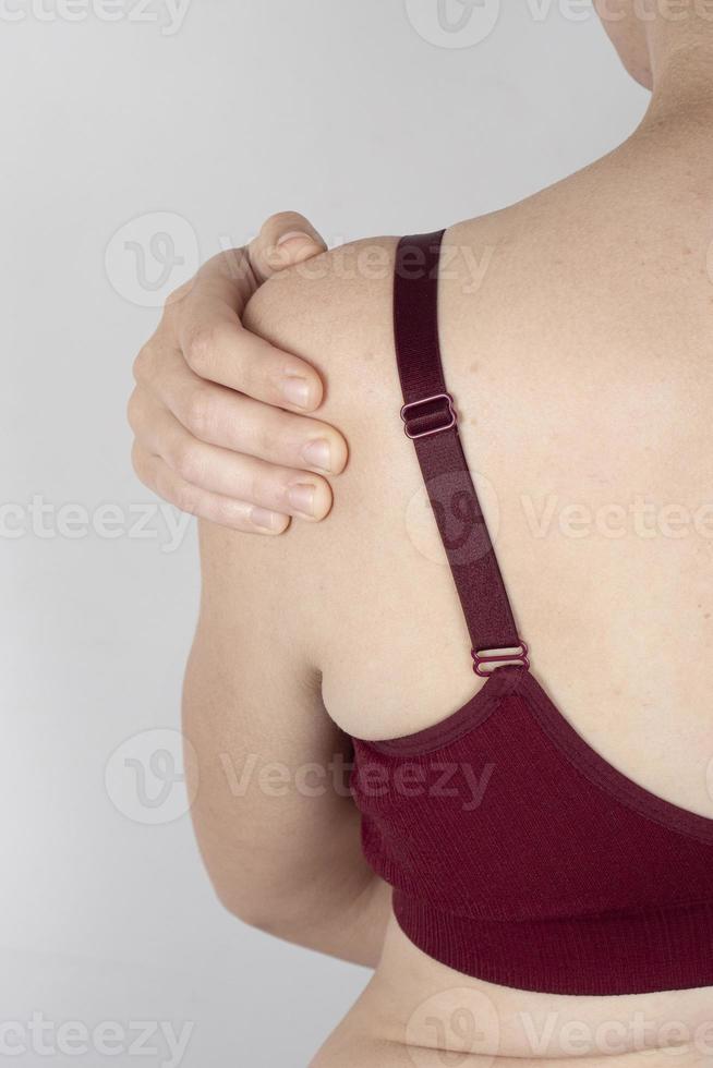 mulher em um sutiã esportivo segurando seu ombro dolorido, tendões esticados do antebraço foto