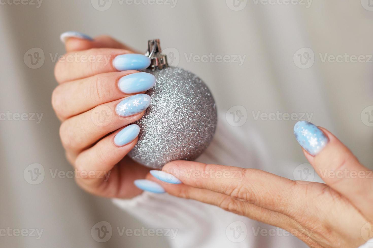 unhas aconchegantes com manicure de inverno com flocos de neve. as mãos da mulher segurando uma bola de brinquedo de natal foto