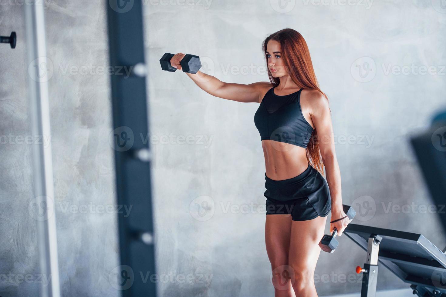 mulher jovem fitness está no ginásio com halteres nas mãos foto