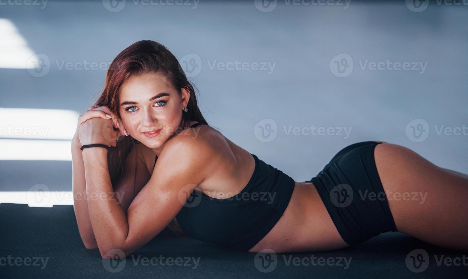 jovem mulher com corpo magro e em roupas esportivas pretas, deitada no colchonete foto