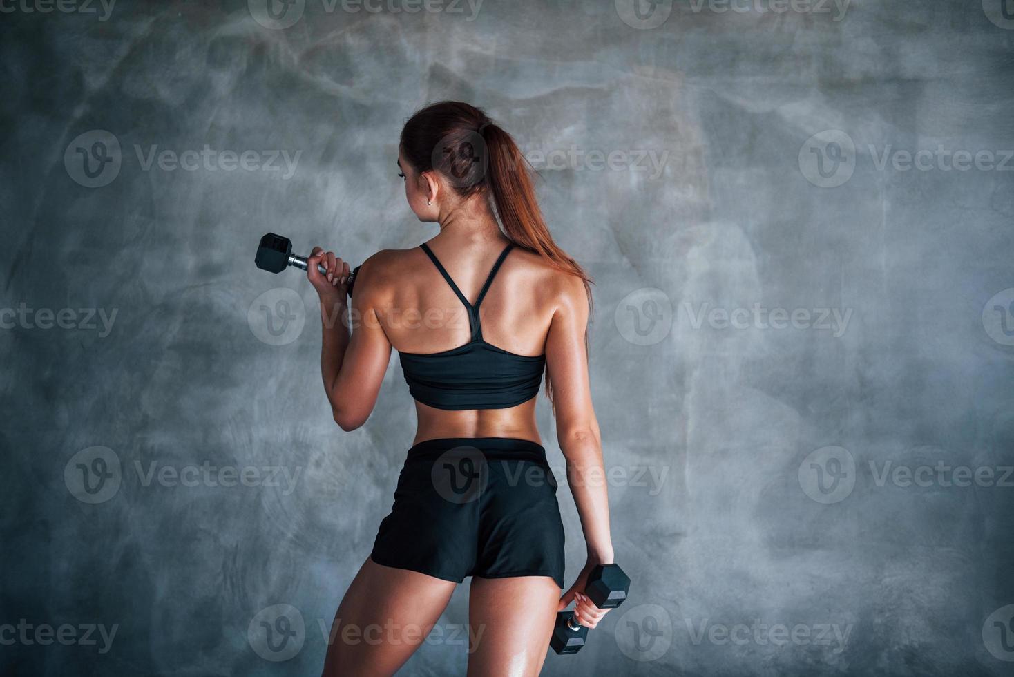 mulher jovem fitness está no ginásio perto da parede com halteres nas mãos foto