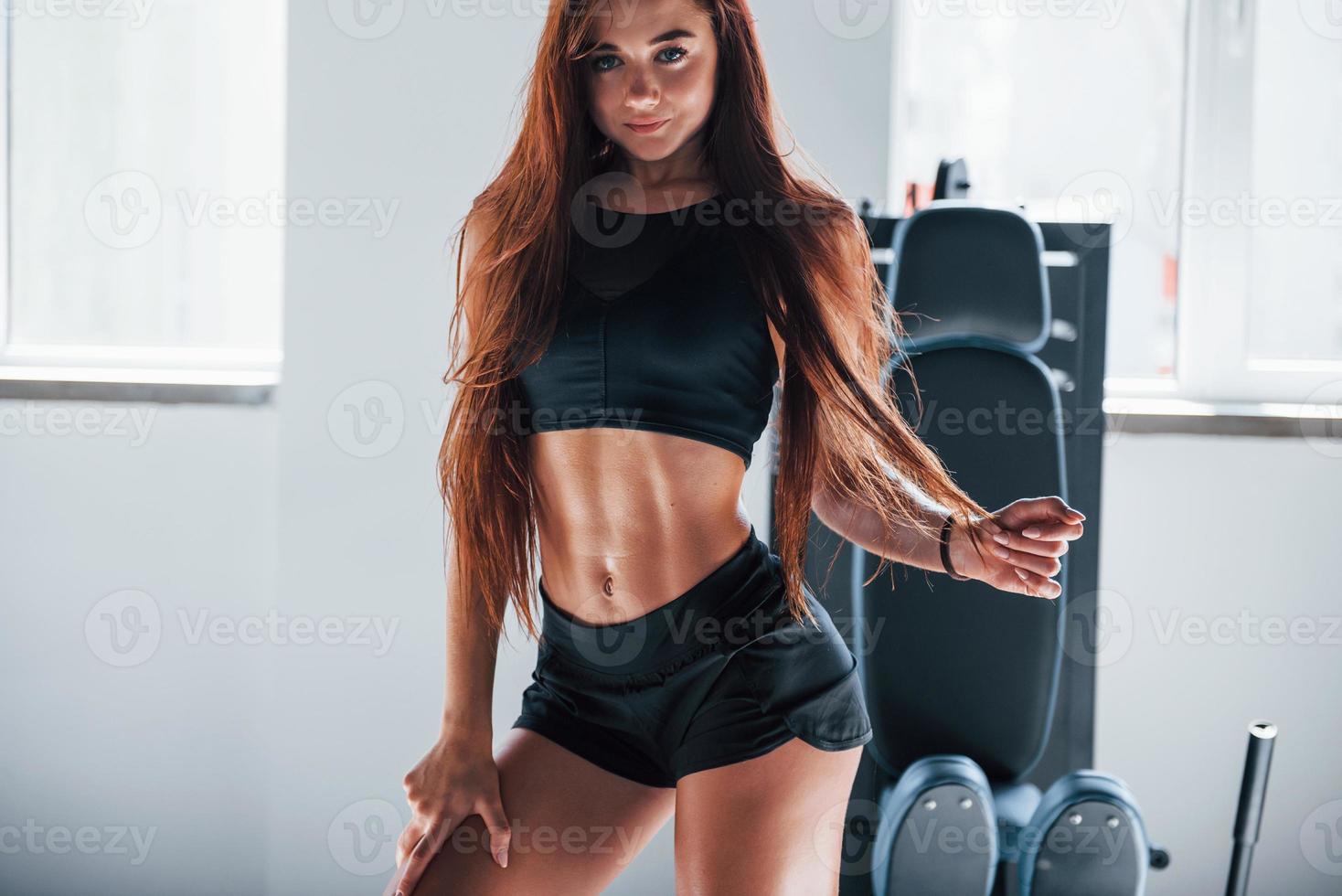 posando para a câmera. mulher jovem fitness com corpo magro e em roupas esportivas pretas está no ginásio foto