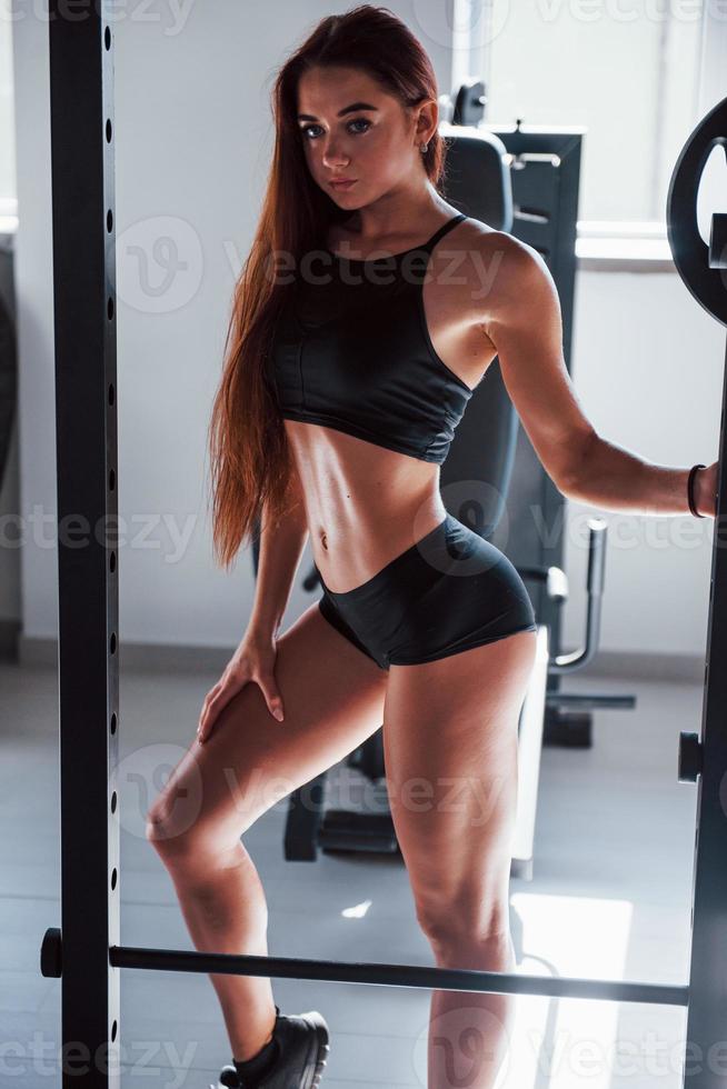 posando para a câmera. mulher jovem fitness com corpo magro e em roupas esportivas pretas está no ginásio foto