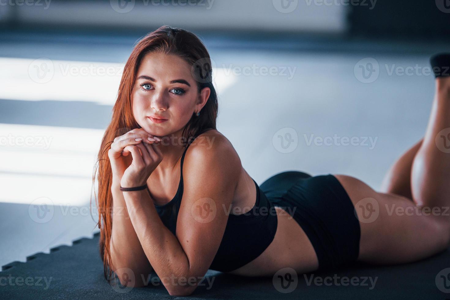 jovem mulher com corpo magro e em roupas esportivas pretas, deitada no colchonete foto