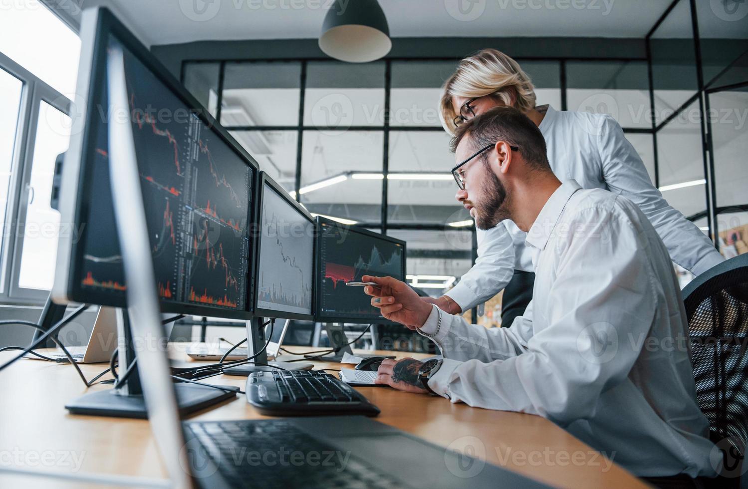 analisando as informações em conjunto. dois corretores em roupas formais trabalham no escritório com mercado financeiro foto