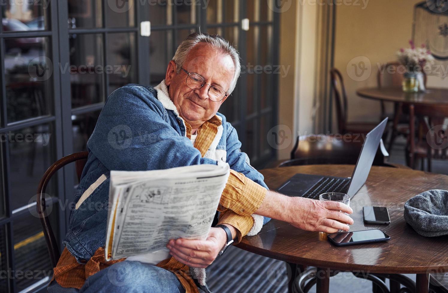 elegante sênior em roupas da moda e óculos senta-se no café e lê jornal foto