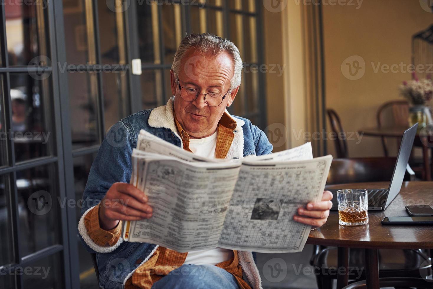 elegante sênior em roupas da moda e óculos senta-se no café e lê jornal foto