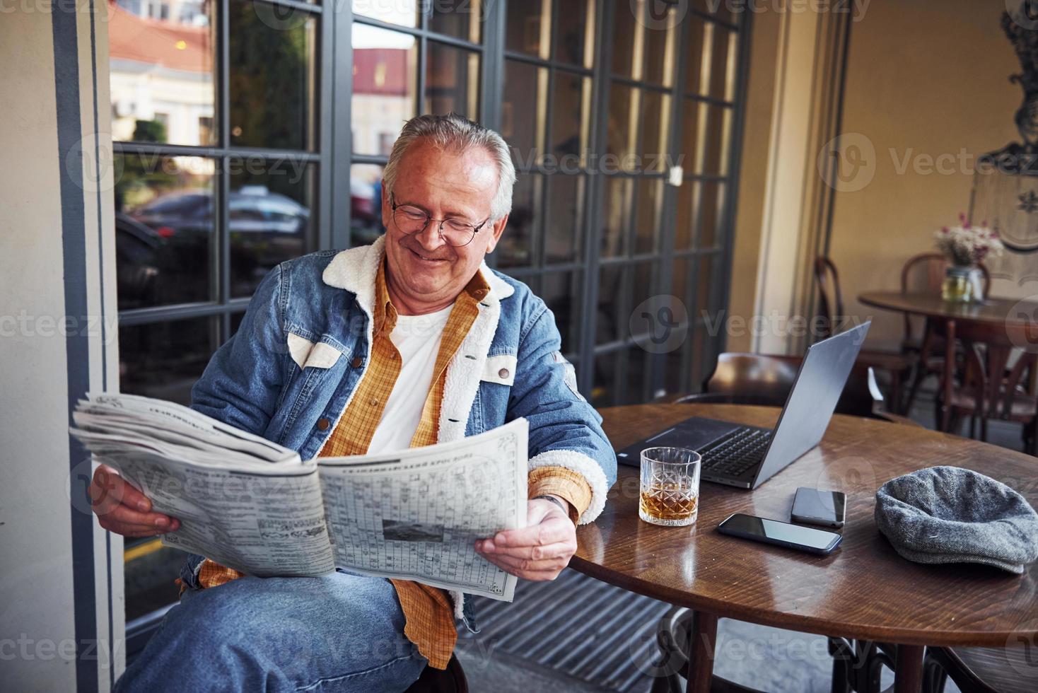 elegante sênior em roupas da moda e óculos senta-se no café e lê jornal foto