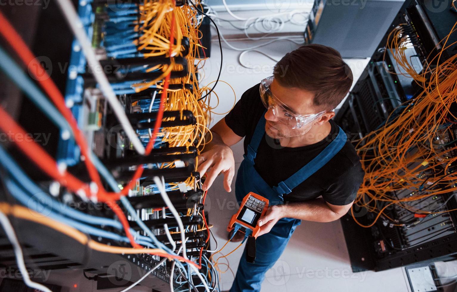 vista superior do jovem de uniforme com dispositivo de medição que funciona com equipamentos de internet e fios na sala do servidor foto