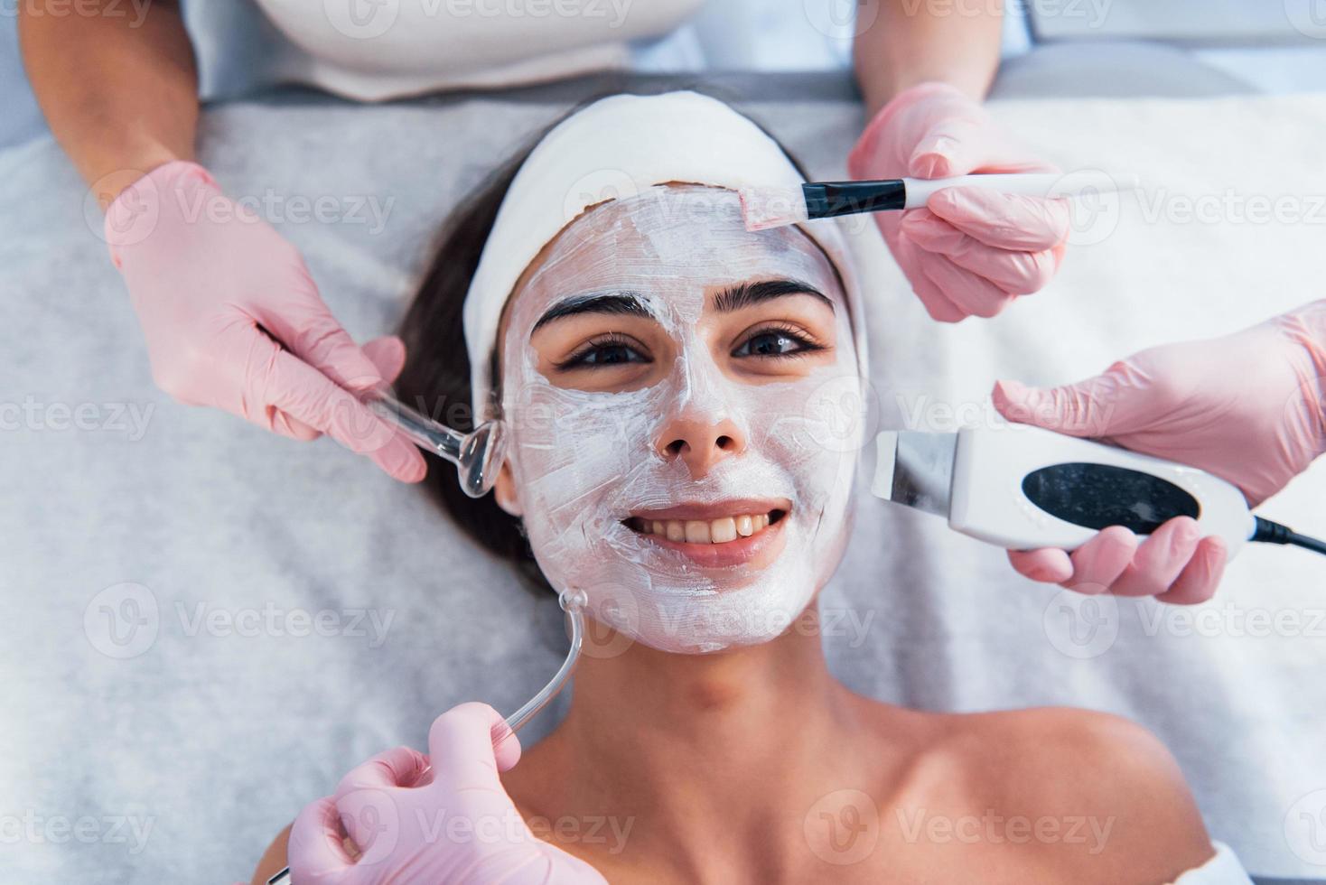 visão aproximada da mulher que está deitada no salão spa e tem procedimento de limpeza facial por diferentes dispositivos e máscara foto
