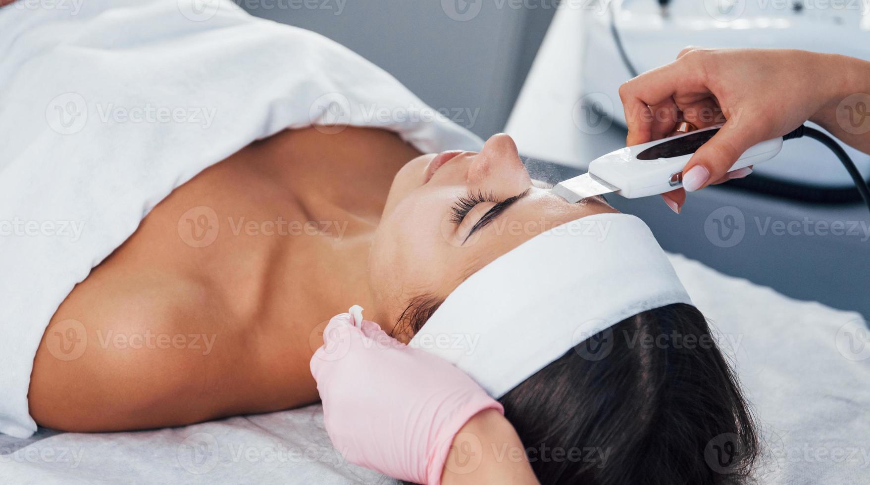 usando dispositivo especial. close-up vista da mulher que está deitada no salão spa e tem procedimento de limpeza facial foto