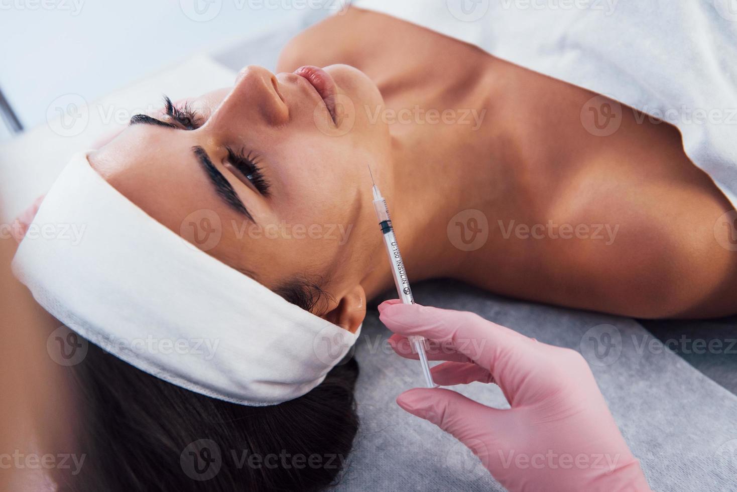 close-up vista da mulher que está deitada no salão spa e tem injeção pela seringa na pele do rosto foto