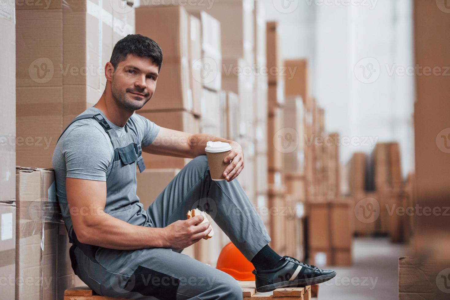 trabalhador de armazenamento senta-se e faz uma pausa. come sanduíche e bebe café foto
