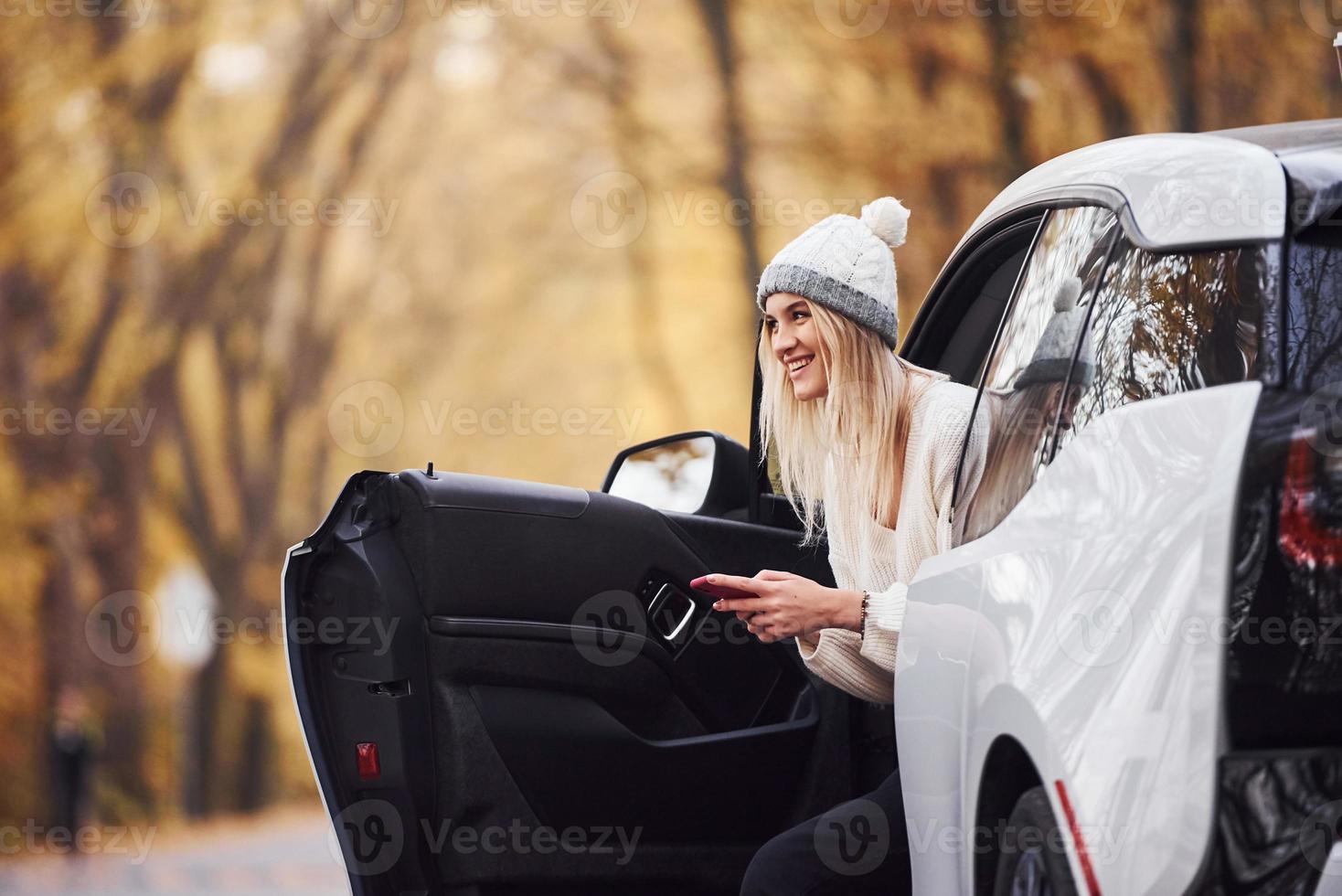 usando smartphones. menina tem viagem de outono de carro. automóvel novo e moderno na floresta foto